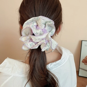Detailed view of a purple floral lace scrunchie styled on a model's hair in a cozy room