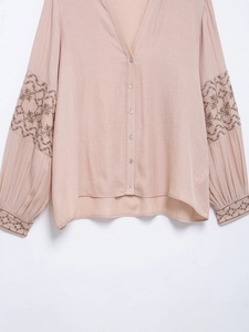 Detail of pink embroidered sleeve and cotton linen fabric texture on V-neck blouse