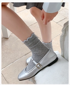 Detail of silver Mary Jane flat shoes paired with grey ruffle mesh socks in ballet style