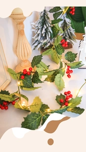 Christmas garland detail with red berries and warm LED lights on a white surface