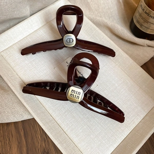 Detail of luxury acrylic hair claws with metal logos on minimalist beige display