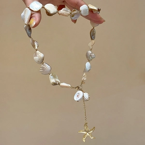 Detail of Y-shaped necklace featuring shell beads and a textured golden starfish charm