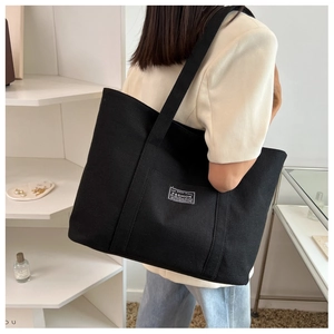 Side view of a large black canvas tote bag with fashion label on female model