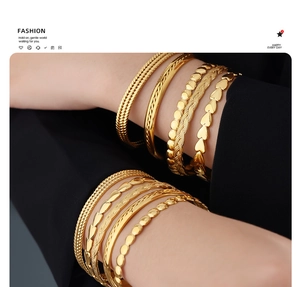 Close-up of a stacked 18k gold-plated bangle and chain bracelet set on a wrist