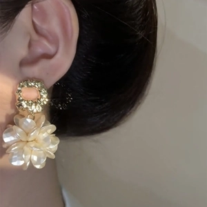 Close-up of gold-plated textured hoop and pearl-like flower earring worn by model