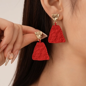 Detailed macro of gold geometric earrings with red trapezoid pendants and hammered texture