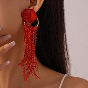 Macro shot of long red beaded fringe earrings with a bold flower stud on a model