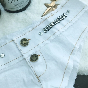 Detail von weißen Denim-Shorts mit Strassbesatz und doppelten Metallknöpfen