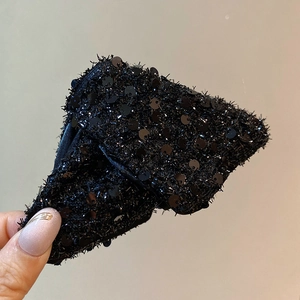 Detail of black bow hair clip with sparkling sequins and textured feather-like fiber finish