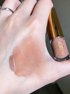 Close-up of sparkling champagne liquid eyeshadow swatched on skin with elegant gold bottle