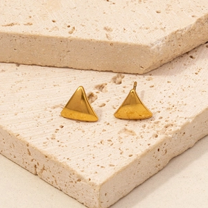 Macro detail of geometric triangle gold stud earrings on minimalist stone texture background