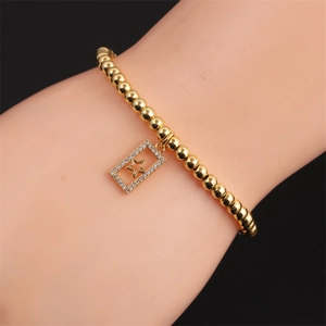 Détail d'un bracelet en perles dorées avec pendentif étoile rectangulaire et zircons blancs