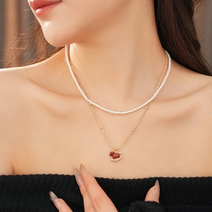 Detail of double-layer gold necklace with pearls and a red horse pendant on neck