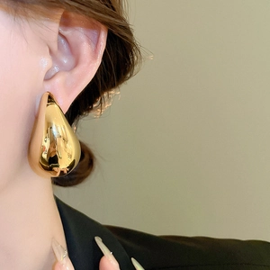 Close-up of model wearing large gold water-drop earrings with a high-shine metal finish