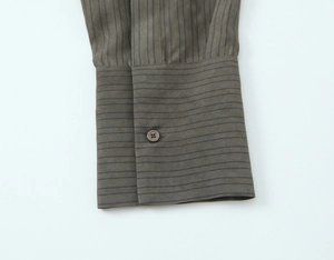 Detail view of the single-button cuff on a gray-brown striped long sleeve shirt