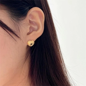 Close-up of golden heart earring with ribbed texture worn by a model on plain background