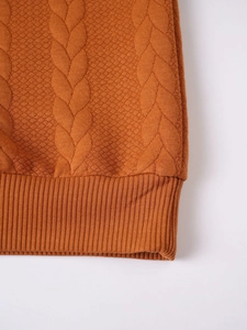 Macro shot of orange cable knit texture and ribbed hem detail on a men's warm sweater