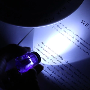 Purple mini LED flashlight keychain lighting a book page in a dark environment