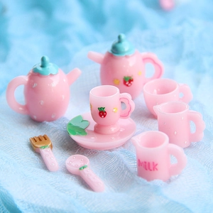 Miniature pink strawberry resin tea set with teapot and cups on light blue background