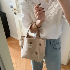 Detail of beige corduroy handbag featuring cute bear embroidery and dual handles