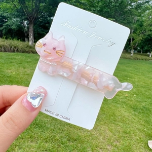 Pink marble acetate cat hair clip with pearl detail held against an outdoor background