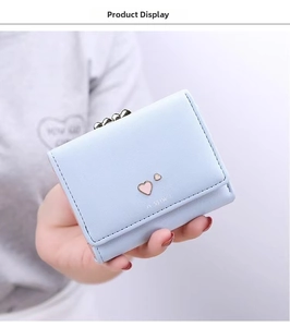 Detail of light blue mini wallet with metal heart clasp held by hand for scale