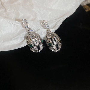 Macro shot of silver snake earrings with pavé crystals and green gem eyes on white texture