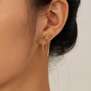 Close-up of golden bow-shaped stainless steel earring worn on an ear for detail view