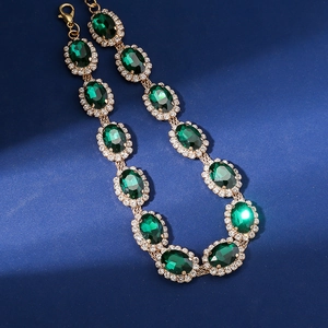 Detailed view of green oval gemstones surrounded by white rhinestones on a gold necklace