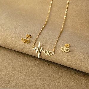 Detailed view of gold heartbeat and double heart necklace and earrings set on textured base