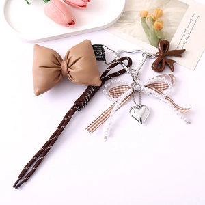 Detailed view of a brown leather phone strap with pearl bow and silver heart pendant