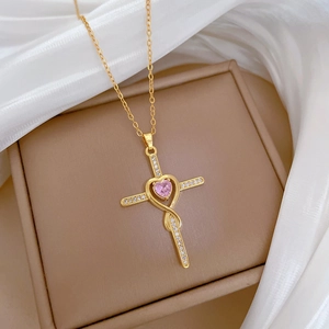 Close-up of golden cross pendant with pink heart gemstone and pavé diamonds on silk