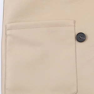 Macro detail of beige faux leather jacket featuring fine stitching and black button
