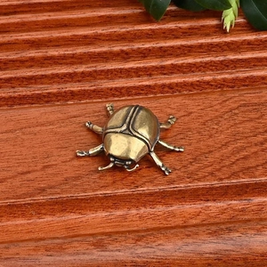 Figura de mariquita vintage de latón en madera oscura con detalle de planta verde