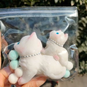 Close-up of soft white flocked cat squishy toys in hand with a blue pompom