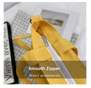 Close-up of smooth silver metal zipper on bright yellow canvas crossbody tote bag