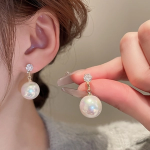 Detail of gold-plated pearl earring with cubic zirconia stud on ear and hand view