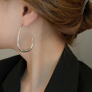Detail of large silver teardrop earrings featuring a sleek polished metallic finish
