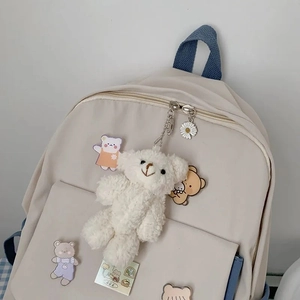 Detail of beige nylon backpack featuring cute plush bear charm and cartoon badges