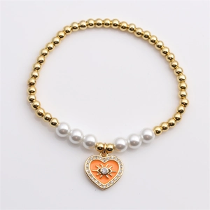 Dettaglio del bracciale elastico con perle dorate e ciondolo a cuore smaltato con occhio