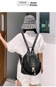 Detailed view of black leather travel backpack with multiple zippers and a cute charm
