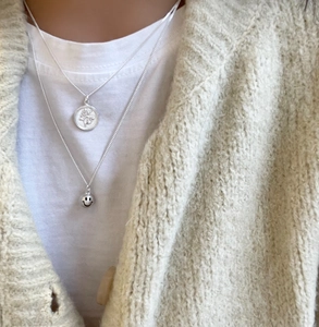 Close-up of layered silver necklace featuring a flower medallion and smiley face pendant