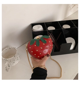 Detailed view of red strawberry shaped crossbody bag with gold chain and green leaf accents