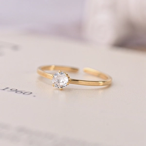 Close-up of golden adjustable ring with a single clear zircon stone on book pages