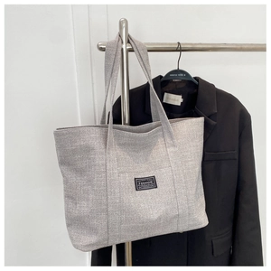 Detail of grey textured fabric tote bag with black decorative patch on silver hanger