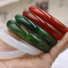 Hand holding five polished agate chalcedony bangles in red, dark green and white colors