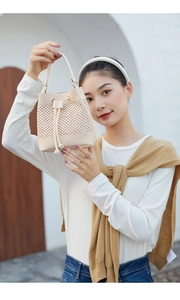 Close-up of cream woven bucket bag with hollow details carried by model outdoors