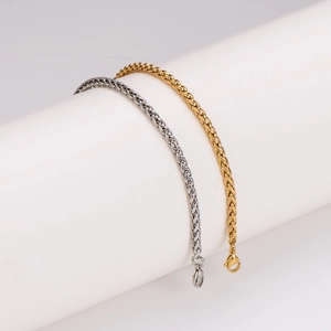 Gold and silver stainless steel spiga wheat chains draped on a white minimalist display