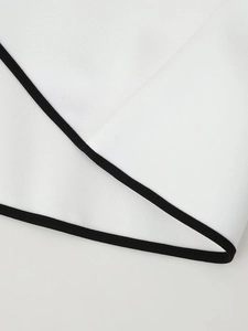 Dettaglio del bordo nero a contrasto su un elegante abito bianco a maniche lunghe in tessuto