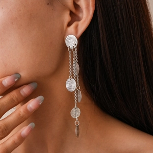 Close-up of model wearing long silver tassel earrings with textured round metal discs